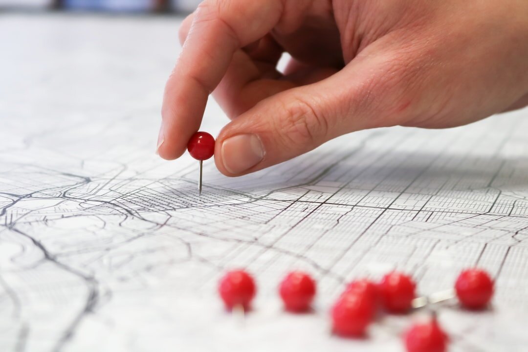 A hand placing red pins on a map to mark target markets